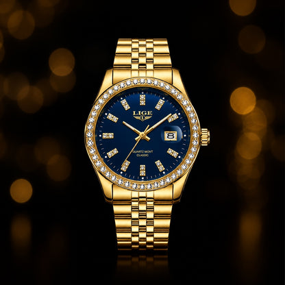 A gold-tone wristwatch with a deep blue dial, a diamond-studded bezel, and a matching gold-tone link bracelet, centered against a dark background with warm golden bokeh lights.